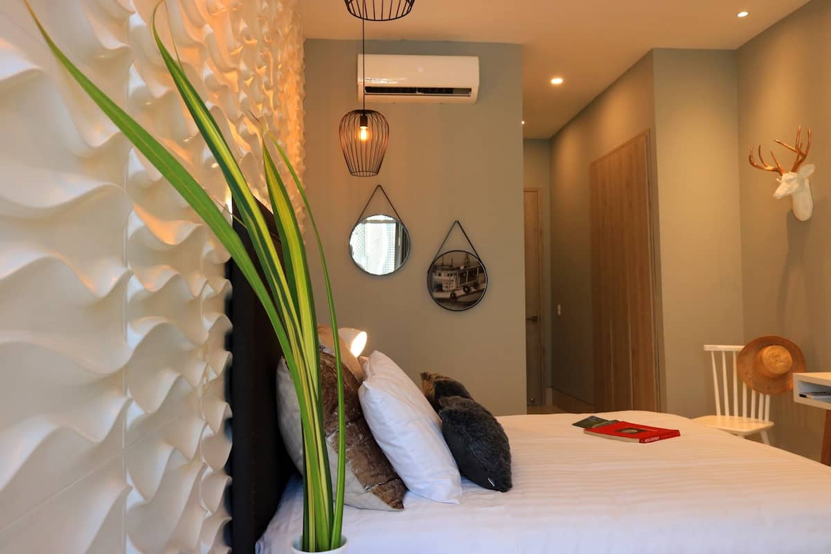 A bedroom with a bed, pillows, a bedside table, a mirror, and a wall-mounted air conditioner.