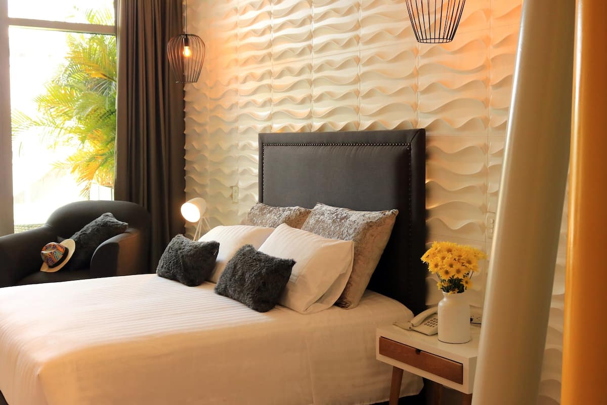 A neatly made bed with a headboard, pillows, and a bedside table with a lamp and a vase of flowers.