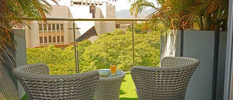 A balcony with wicker chairs, a small table, and a drink.