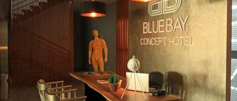 A modern hotel lobby with a wooden reception desk, a mannequin, and a large wall sign reading "BLUEBAY CONCEPT HOTEL."