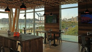 A restaurant with a wooden ceiling, large windows, and a view of a harbor. Tables and chairs are arranged for dining. - Bonita Bay Concept Hotel by Xarm Hotels (Santa Marta)