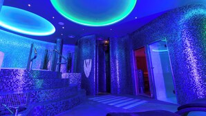 A modern spa room with mosaic tile walls, a circular skylight, and a seating area with a massage table.