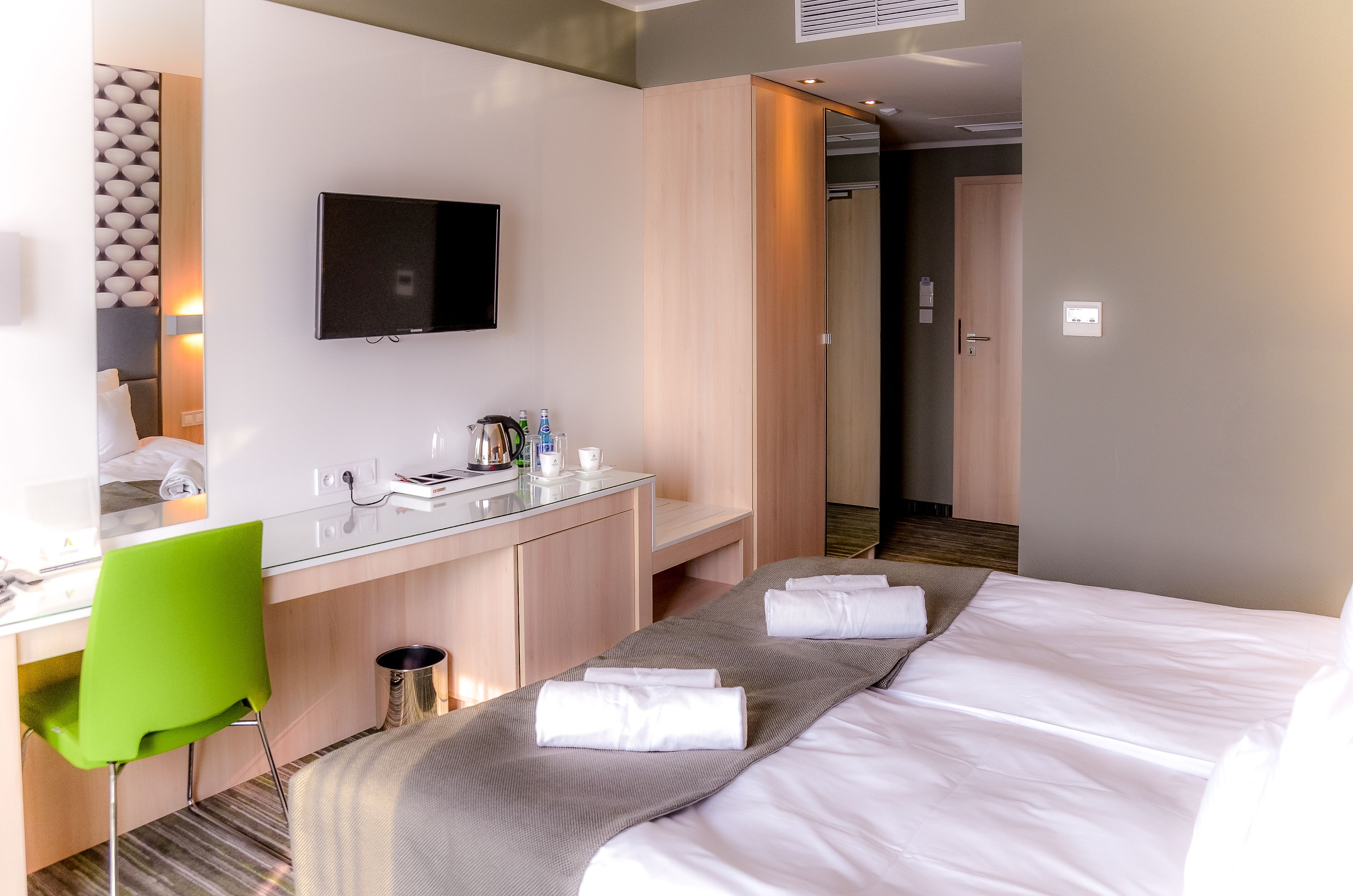 A hotel room with a bed, a desk with a chair, a TV, and a mirror.