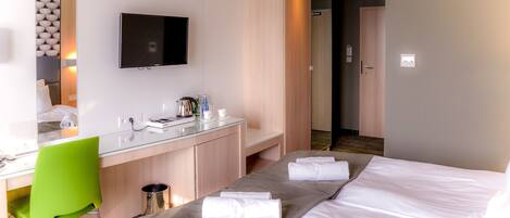 A hotel room with a bed, a desk with a chair, a TV, and a mirror.