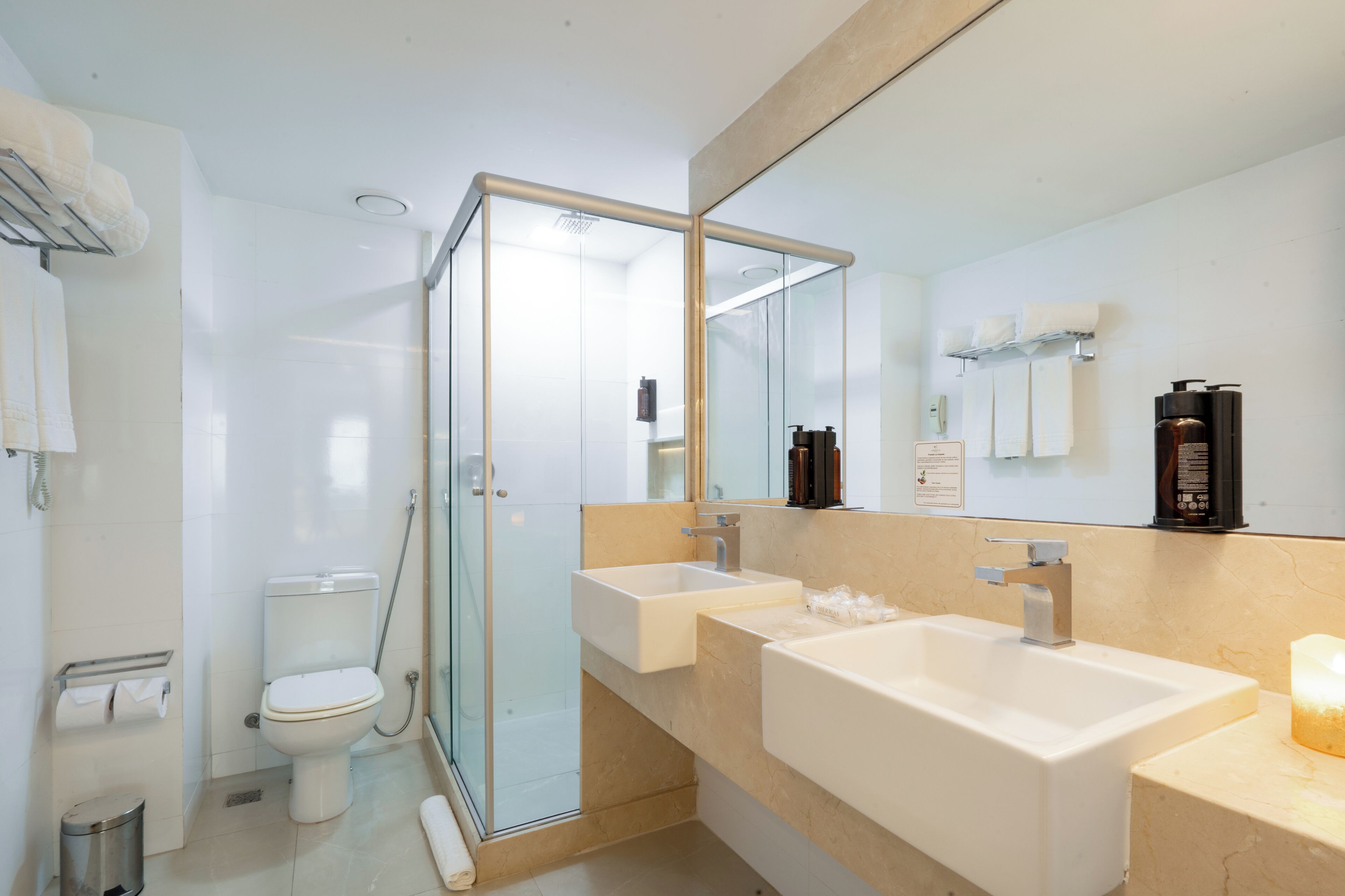 Een moderne badkamer met een douchecabine van glas, een toilet en twee wastafels.