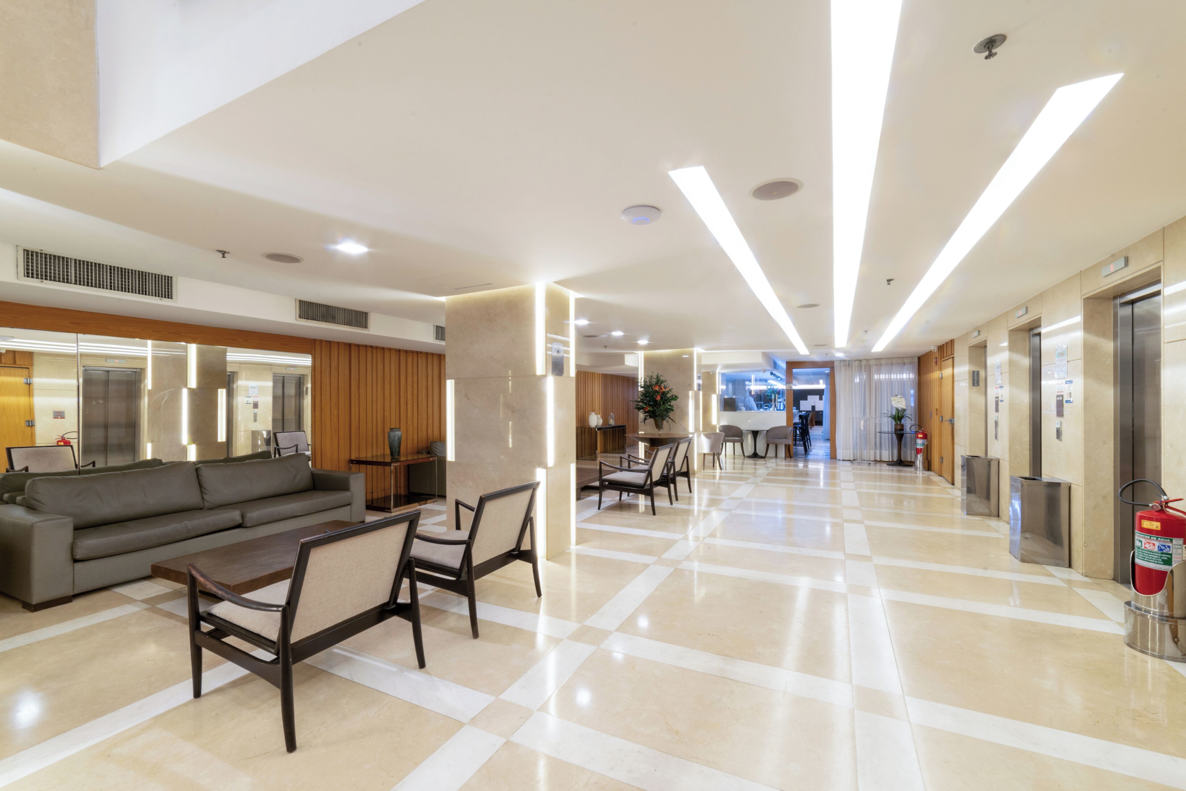 Een moderne lobby met een zwart-wit geruit vloerkleed, een bank, stoelen, een receptiebalie en een lift.