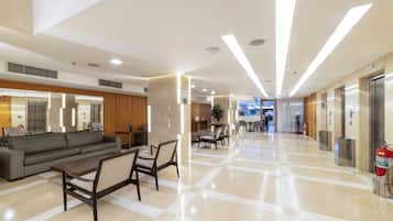 Een moderne lobby met een zwart-wit geruit vloerkleed, een bank, stoelen, een receptiebalie en een lift.