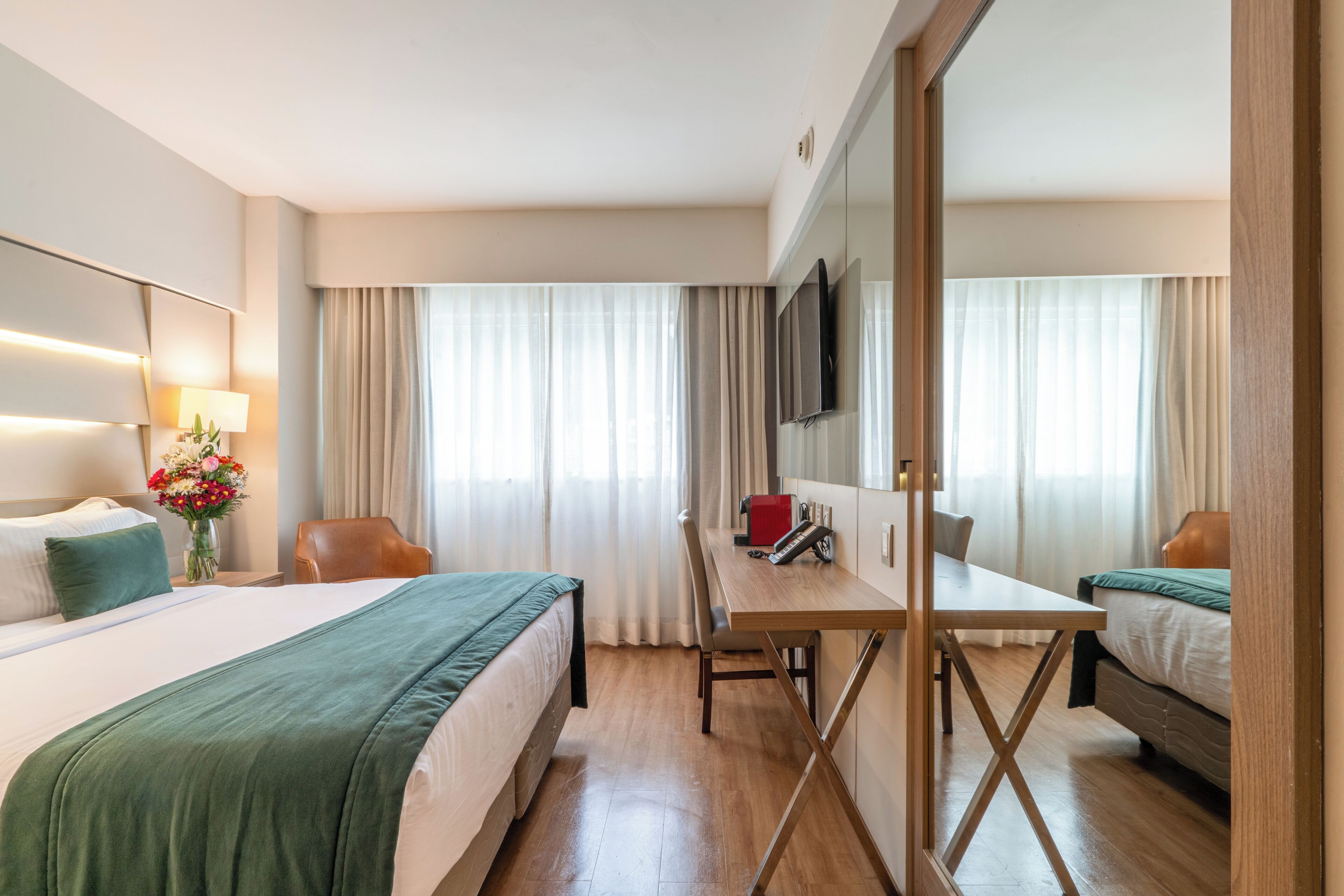 A hotel room with a bed, desk, chair, and a TV.