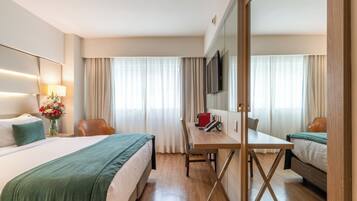 A hotel room with a bed, desk, chair, and a TV.