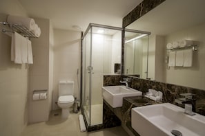 A modern bathroom with a glass-enclosed shower, a toilet, and two sinks.