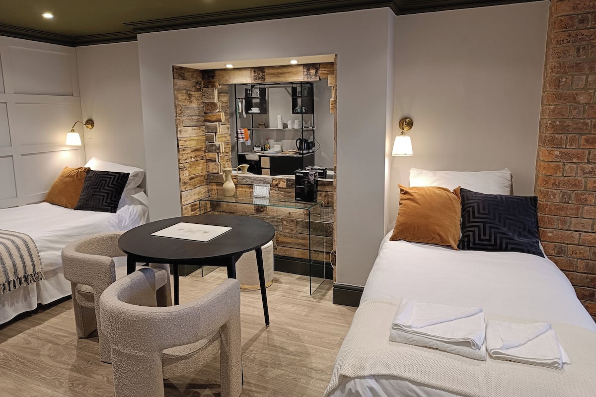A hotel room with two beds, a small table, and a seating area.