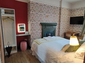 A neatly arranged bedroom with a bed, bedside lamp, and a television mounted on the wall. - Rooms on The Prom (Cheltenham)