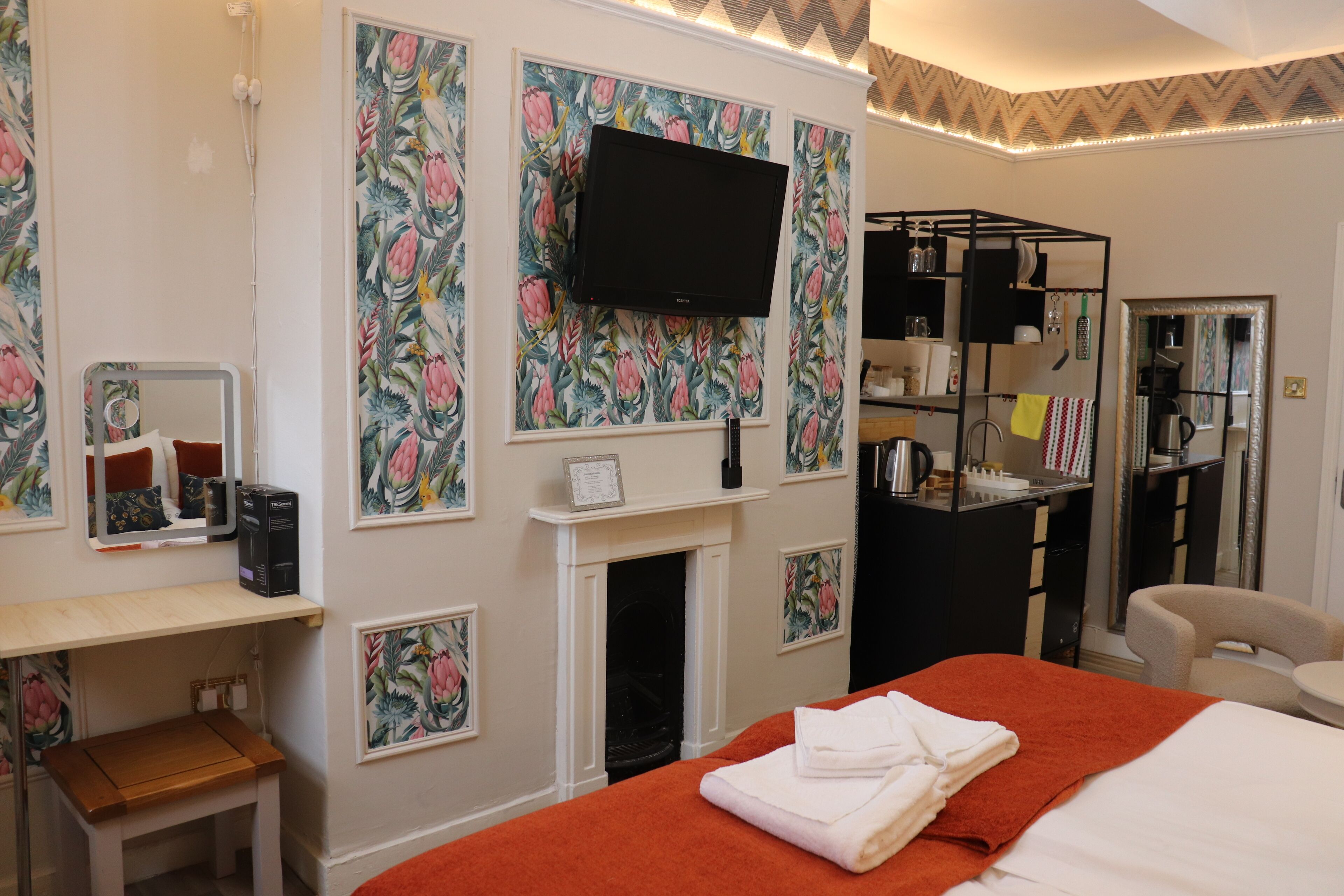 A hotel room with a bed, a TV, a fireplace, a desk, and a mirror.