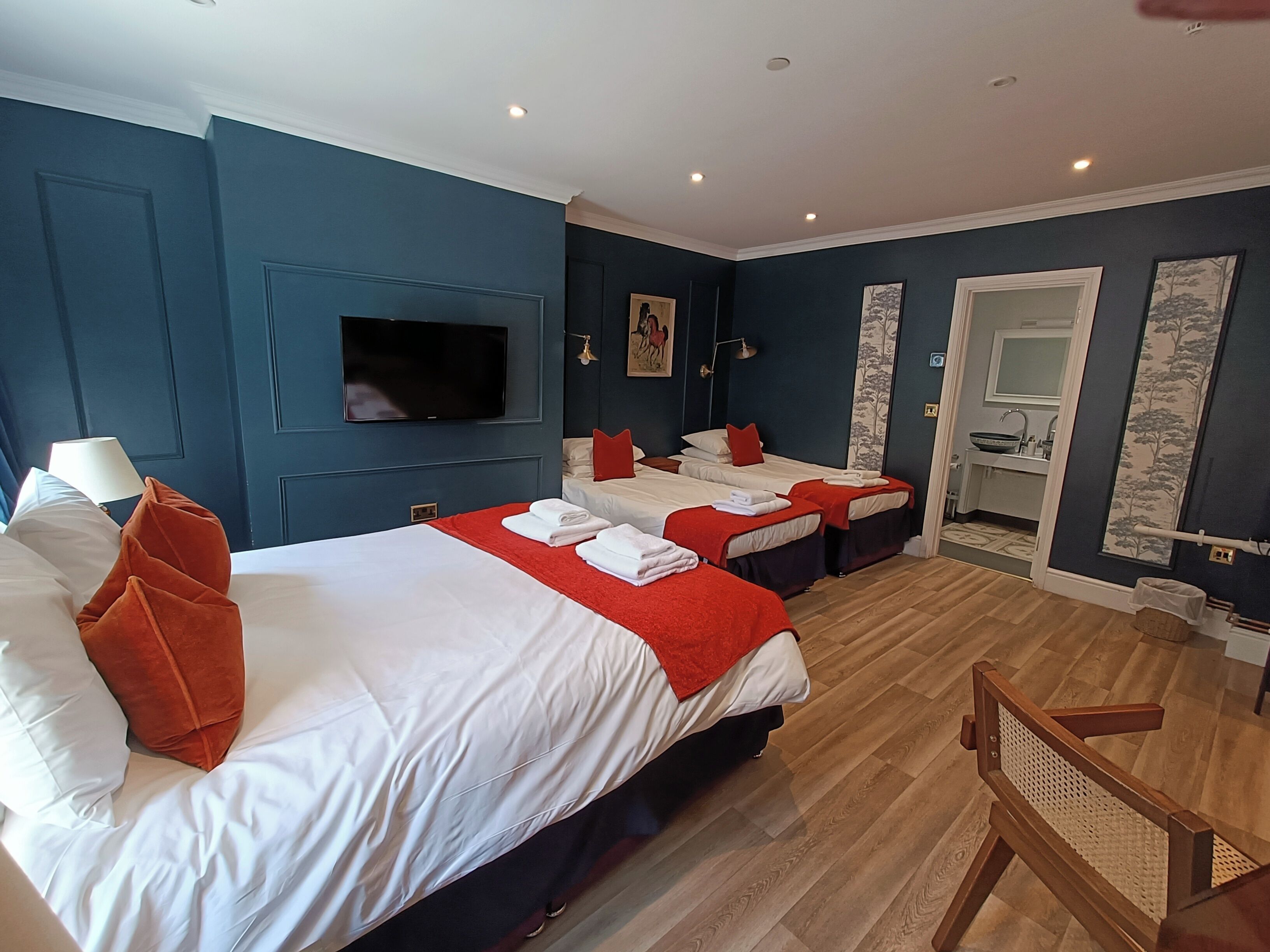 A hotel room with two beds, a TV, a bathroom, and a wooden chair.