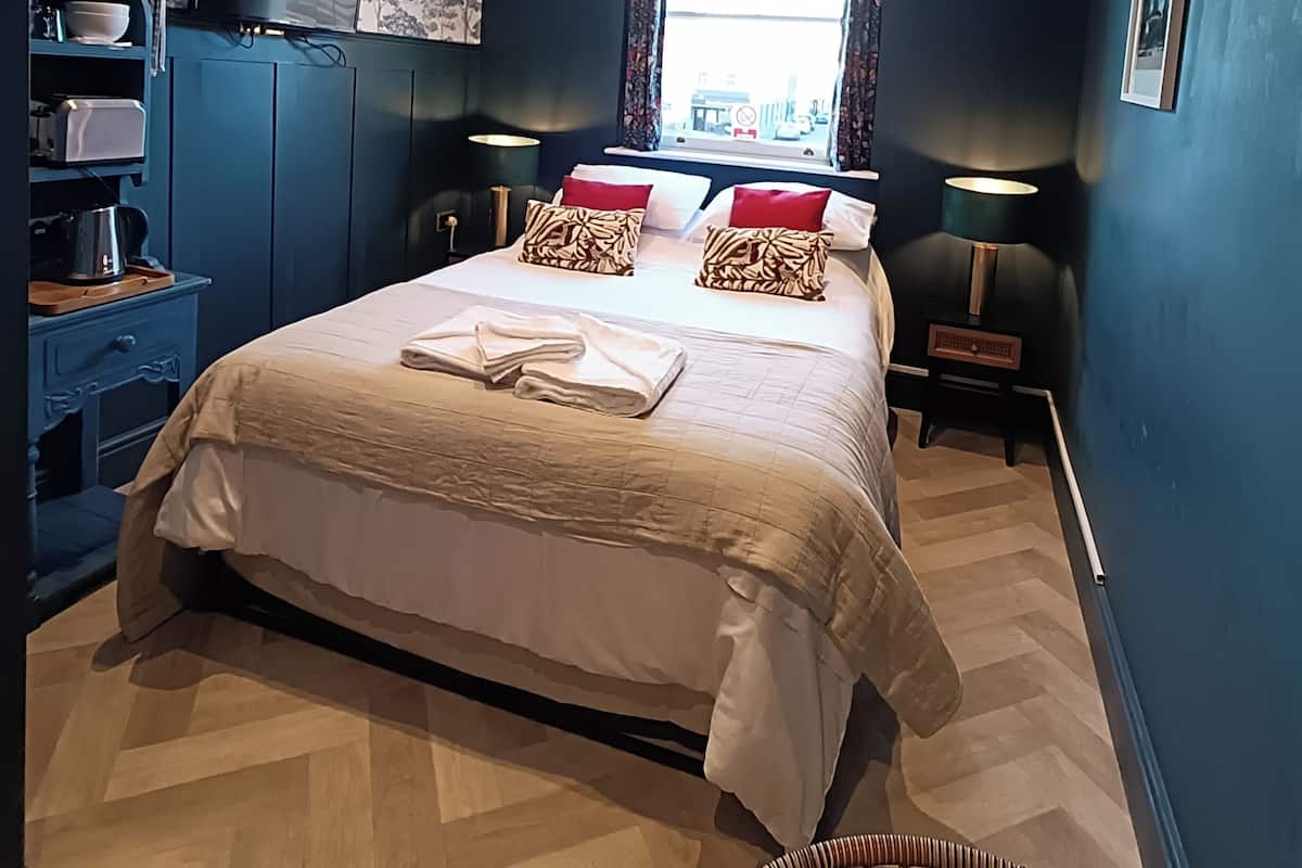 A bedroom with a large bed, a television on a stand, a window with curtains, and a wall-mounted shelf.