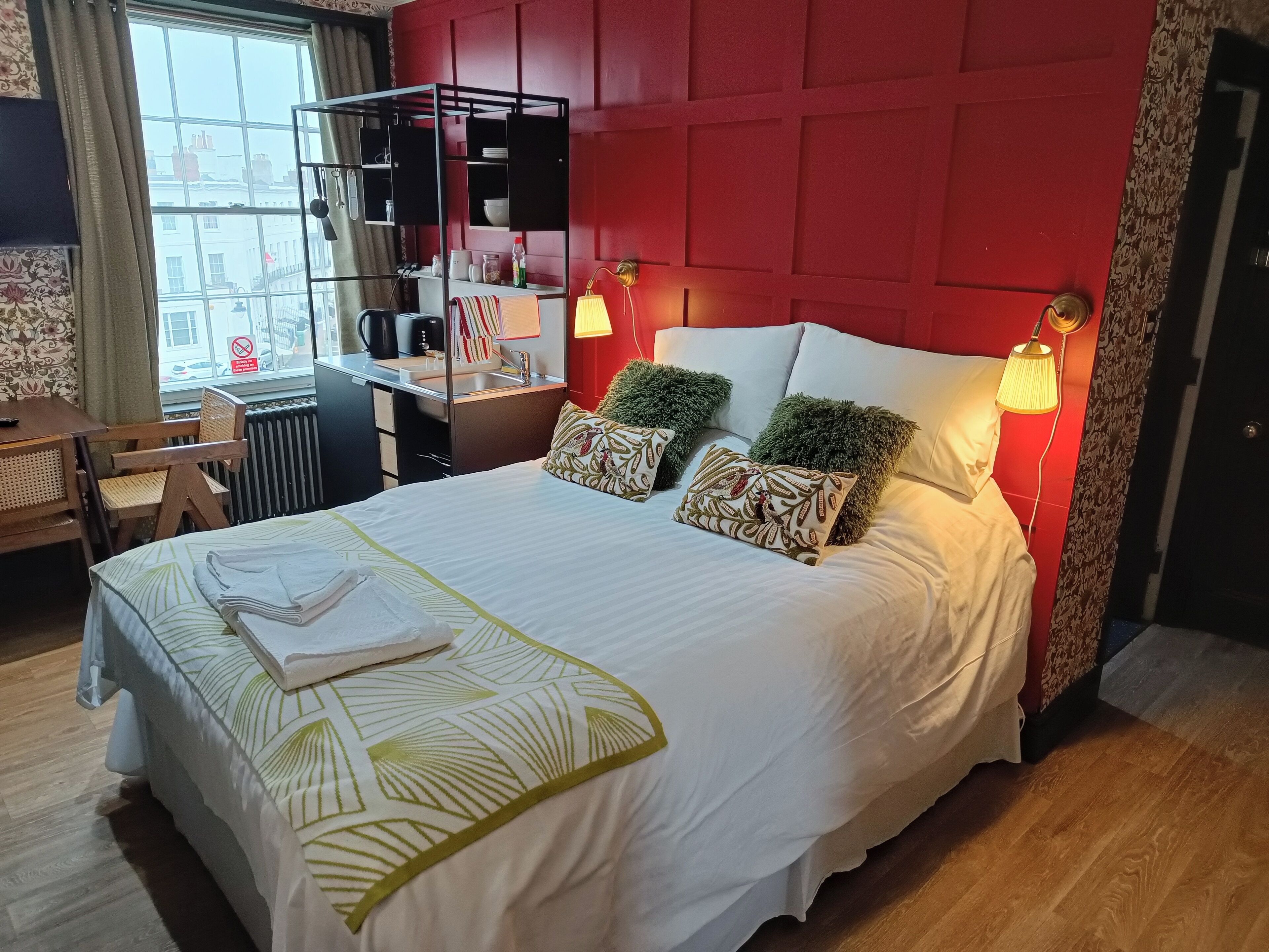 A neatly made bed with a white and green patterned bedspread, two decorative pillows, and two wall-mounted reading lamps.