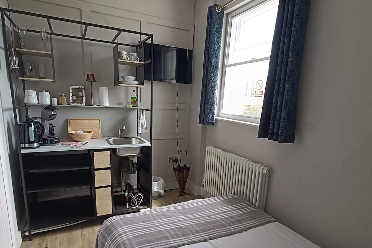 A compact bedroom with a bed, a desk, and a window with curtains.