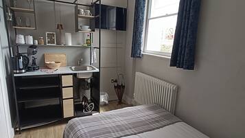Un dormitorio pequeño con cama, escritorio y ventana con cortinas.