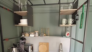 A compact kitchen with a sink, a coffee maker, a toaster, and shelves holding cups and jars. - Rooms on The Prom (Cheltenham)