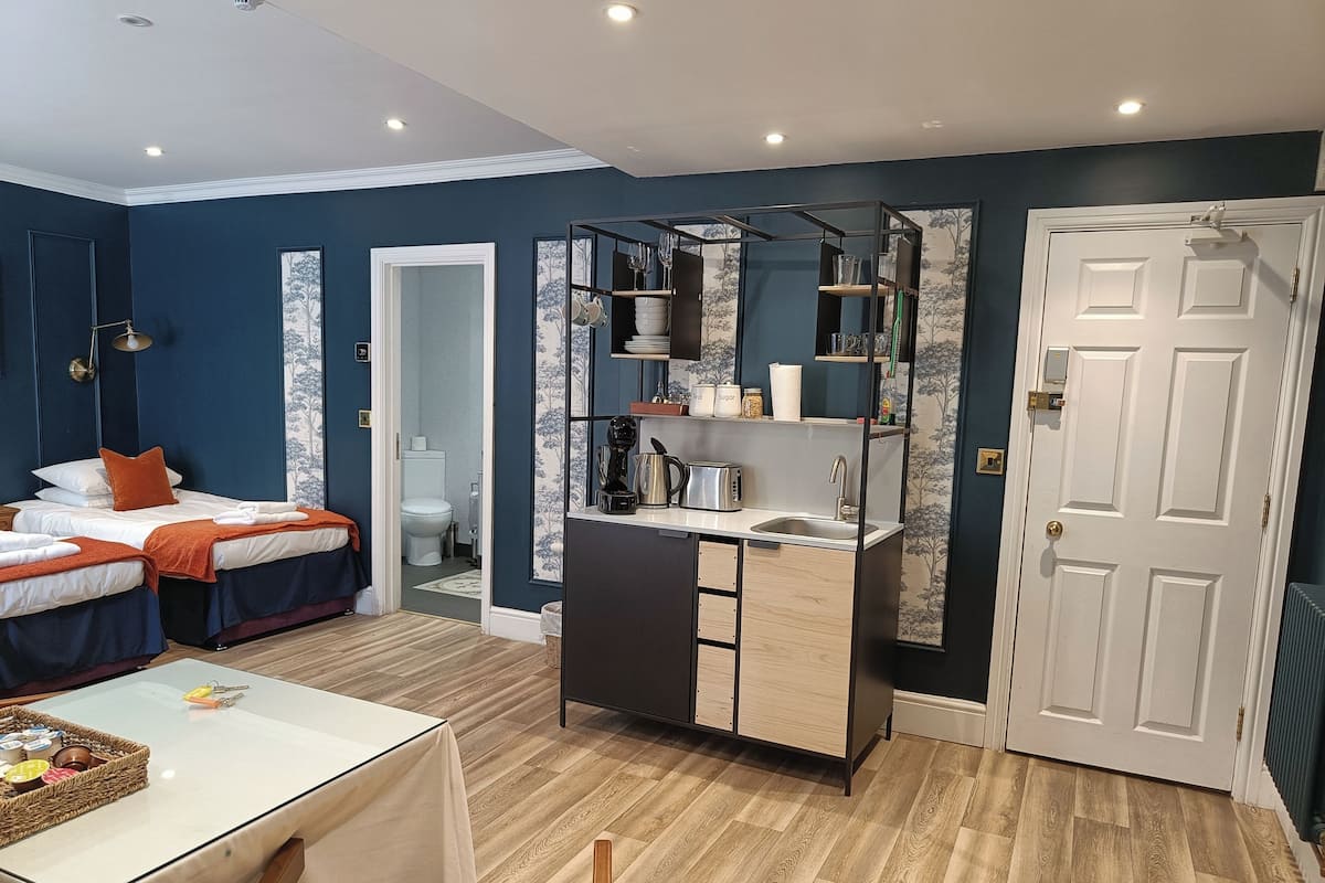 A compact room with a bed, a small kitchenette, a dining table, and a door.
