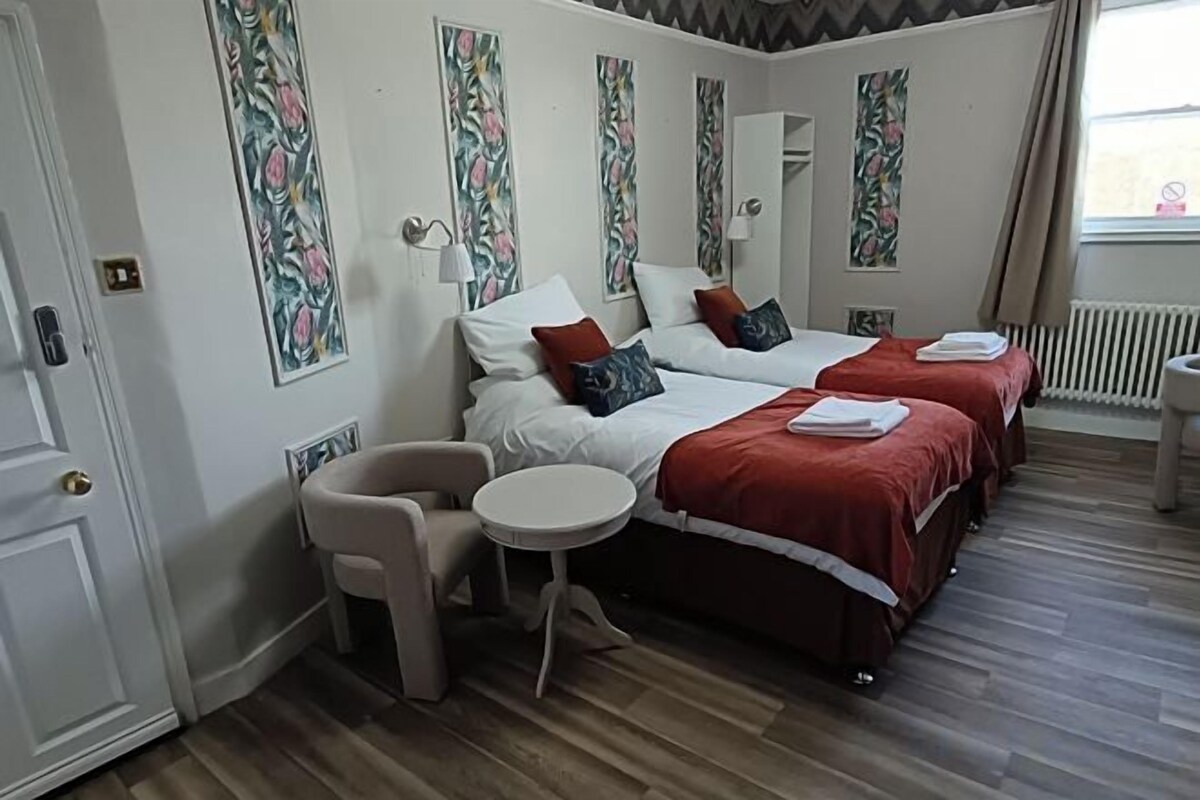 A hotel room with two beds, a small round table, a chair, and a door.