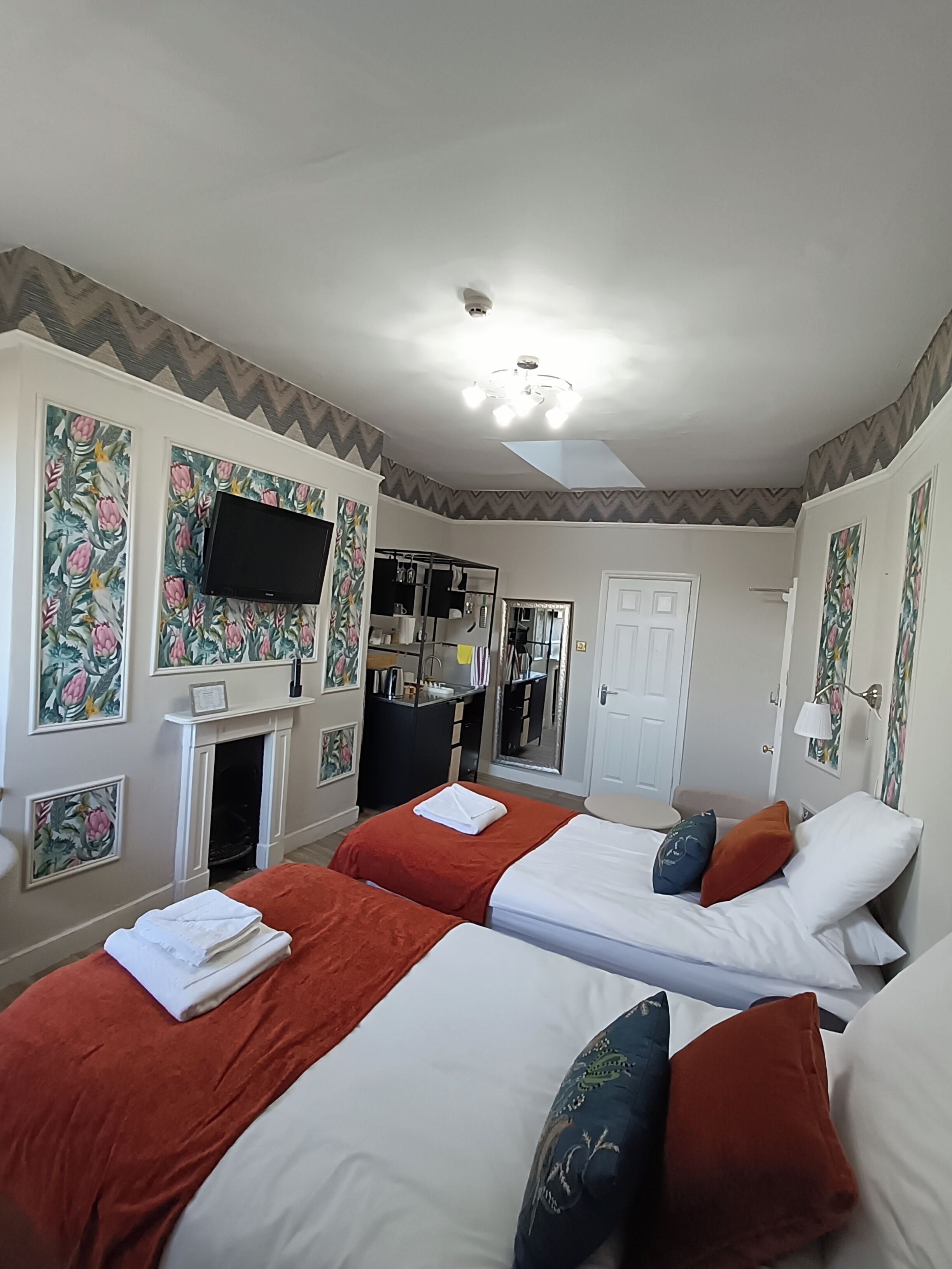 A hotel room with two beds, a flat-screen TV, a fireplace, a mirror, and a door.