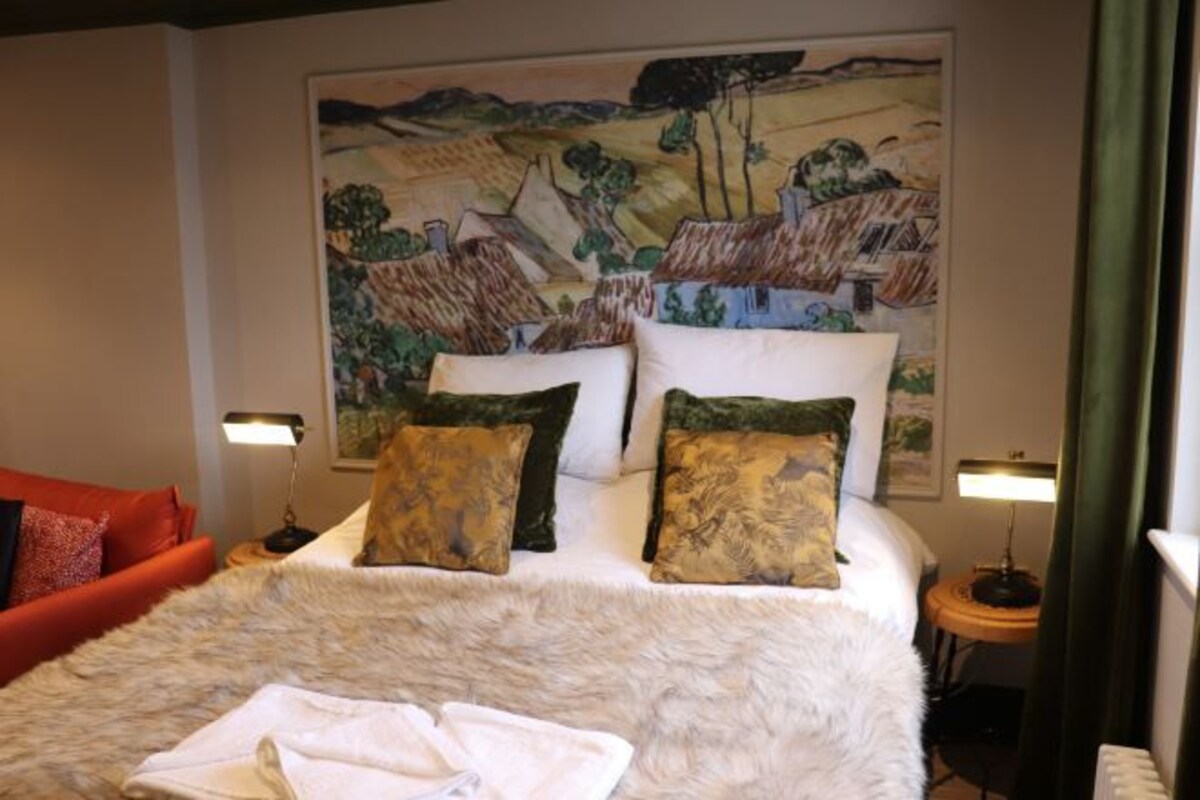 Une chambre d’hôtel avec un grand lit, deux tables de chevet avec des lampes, un canapé rouge et un tableau au mur.