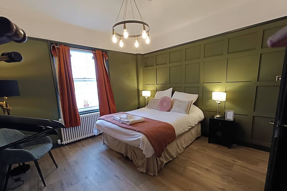 A neatly arranged bedroom with a bed, bedside lamps, a radiator, and a window with curtains.