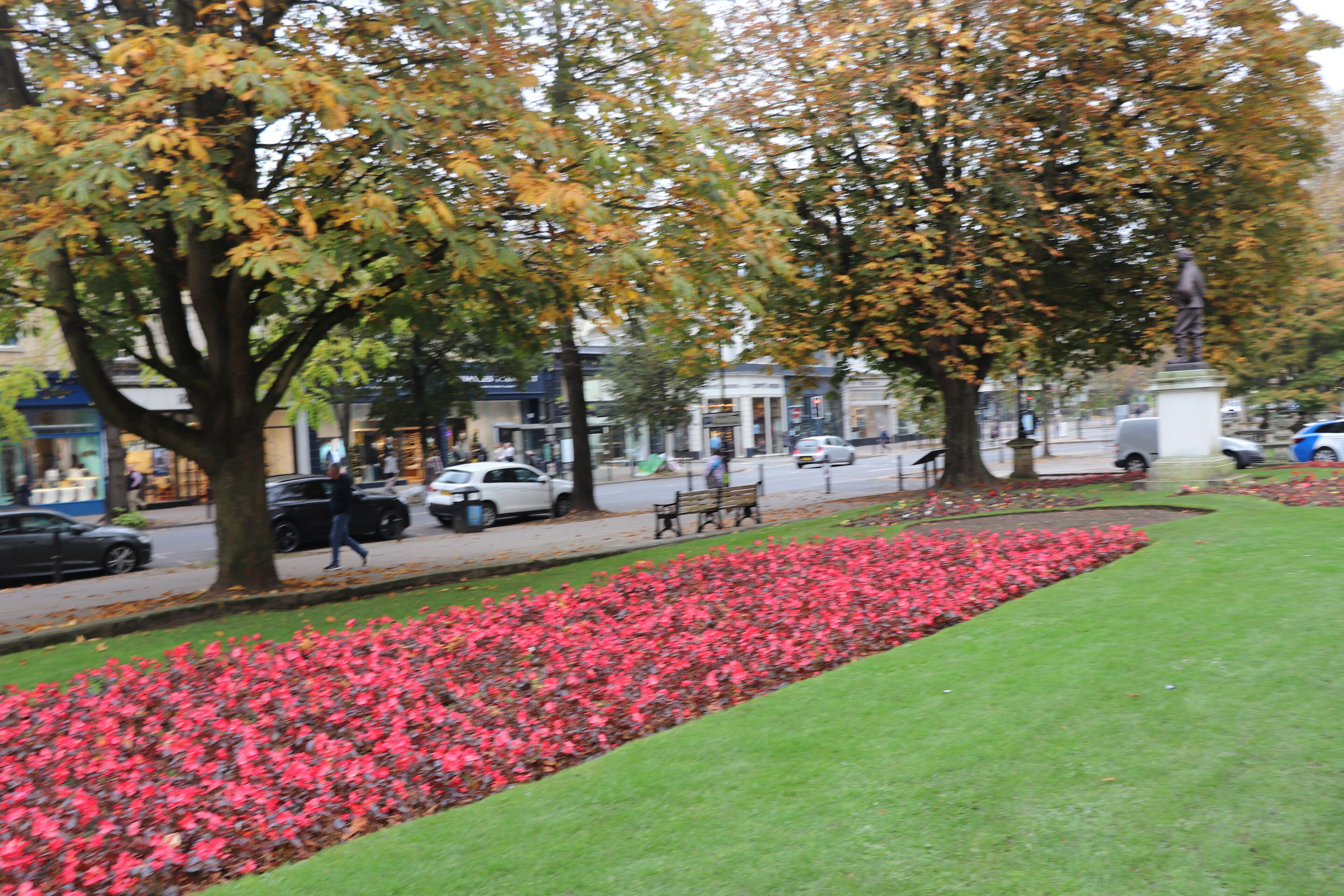 A park with a flower bed, benches, and a statue.