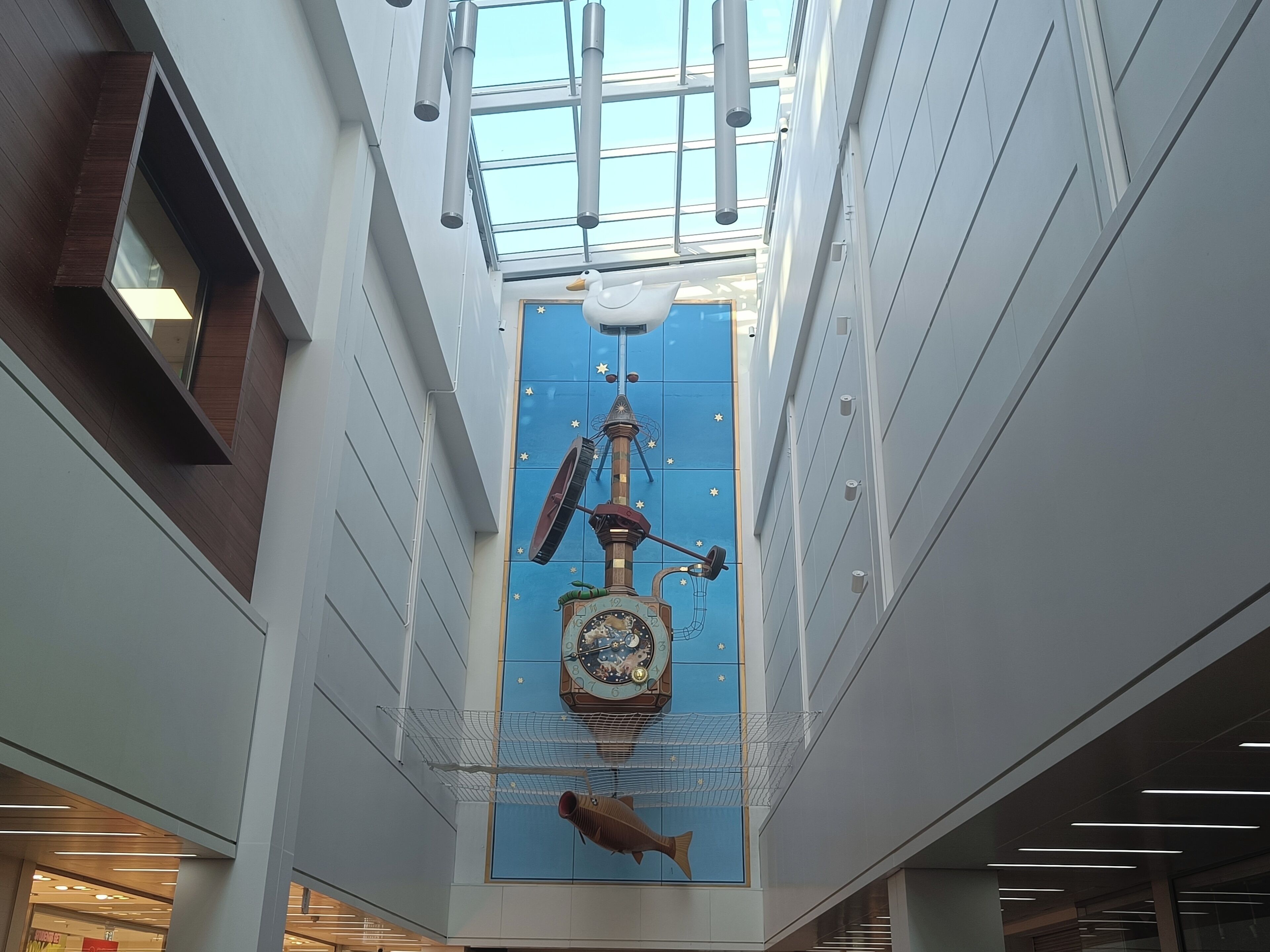 Ein modernes Interieur mit einer zentralen Dekoration – einer Wanduhr, einer hängenden Vogelplastik und einer Fische Skulptur darunter.