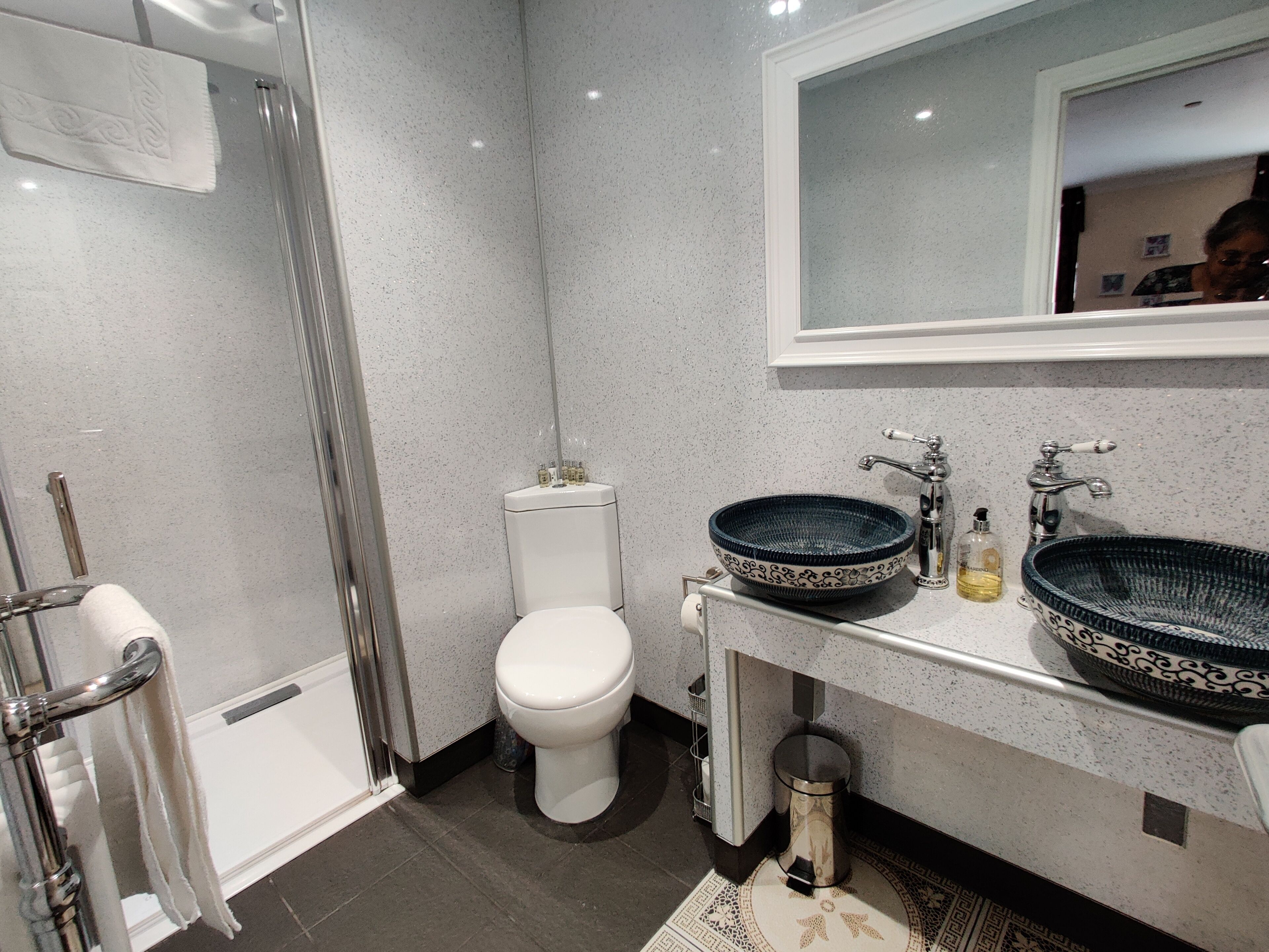 Un baño moderno con ducha envuelta en vidrio, inodoro blanco y lavamanos con un recipiente decorativo.