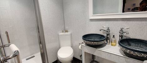 A modern bathroom with a glass-enclosed shower, a white toilet, and a sink with a decorative bowl.