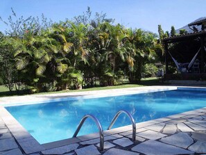 A swimming pool with a stone deck, surrounded by lush greenery and a hammock. - Pousada Serra da Mantiqueira (Pindamonhangaba)