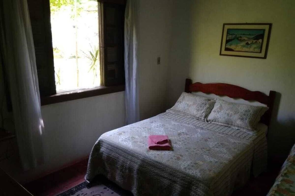 Un dormitorio con cama, ventana con cortinas, un cuadro en la pared y una alfombra estampada en el suelo.
