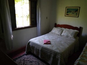 A bedroom with a bed, a window with curtains, a framed picture on the wall, and a patterned rug on the floor. - Pousada Serra da Mantiqueira (Pindamonhangaba)