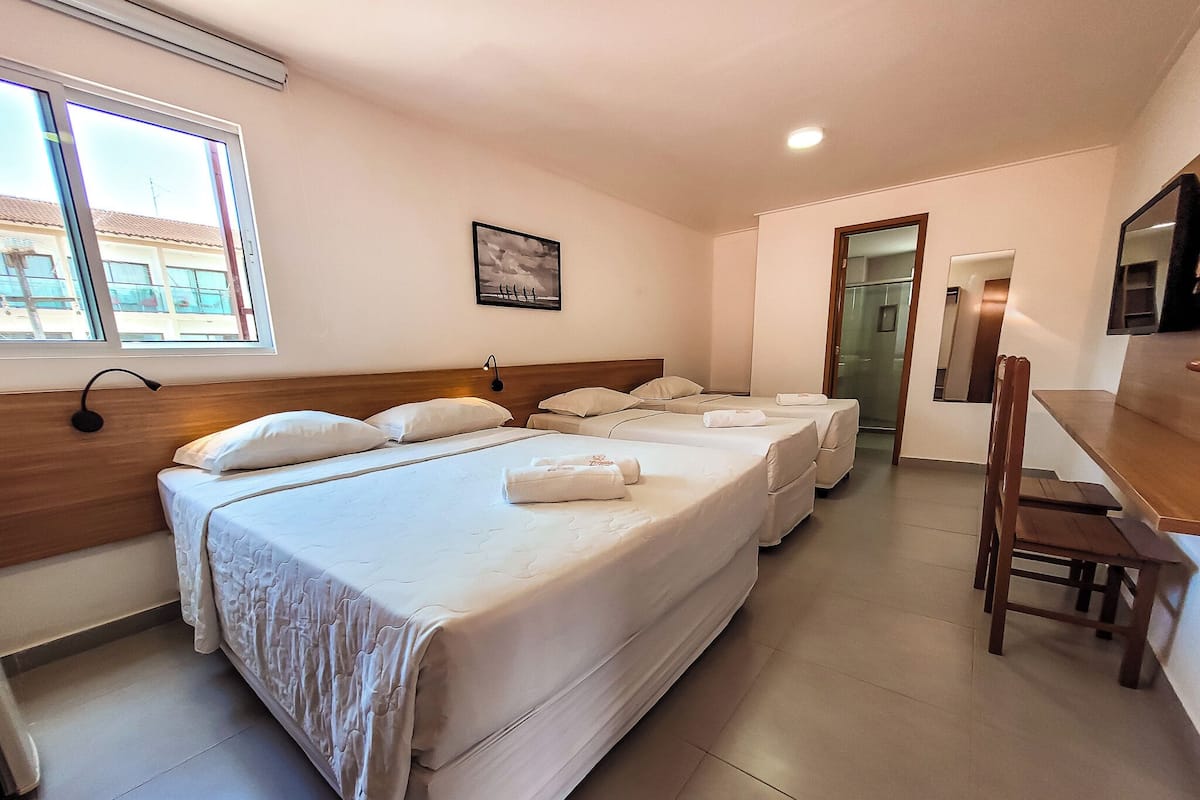 Habitación de hotel con tres camas, un cabecero de madera, un escritorio y una silla.