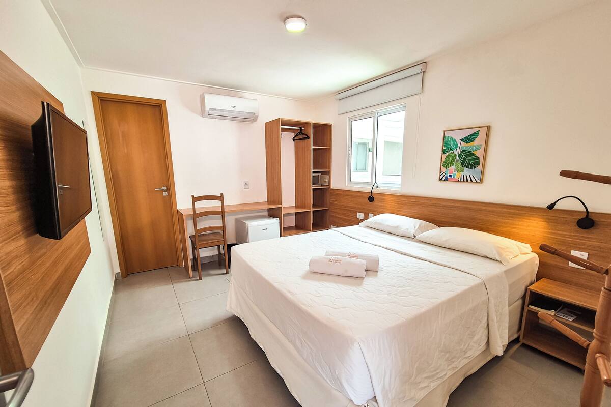 Un dormitorio con cama, escritorio, silla, armario y televisor.