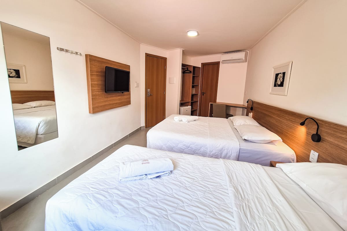 Una habitación de hotel con dos camas, un televisor montado en la pared, un armario y un espejo.