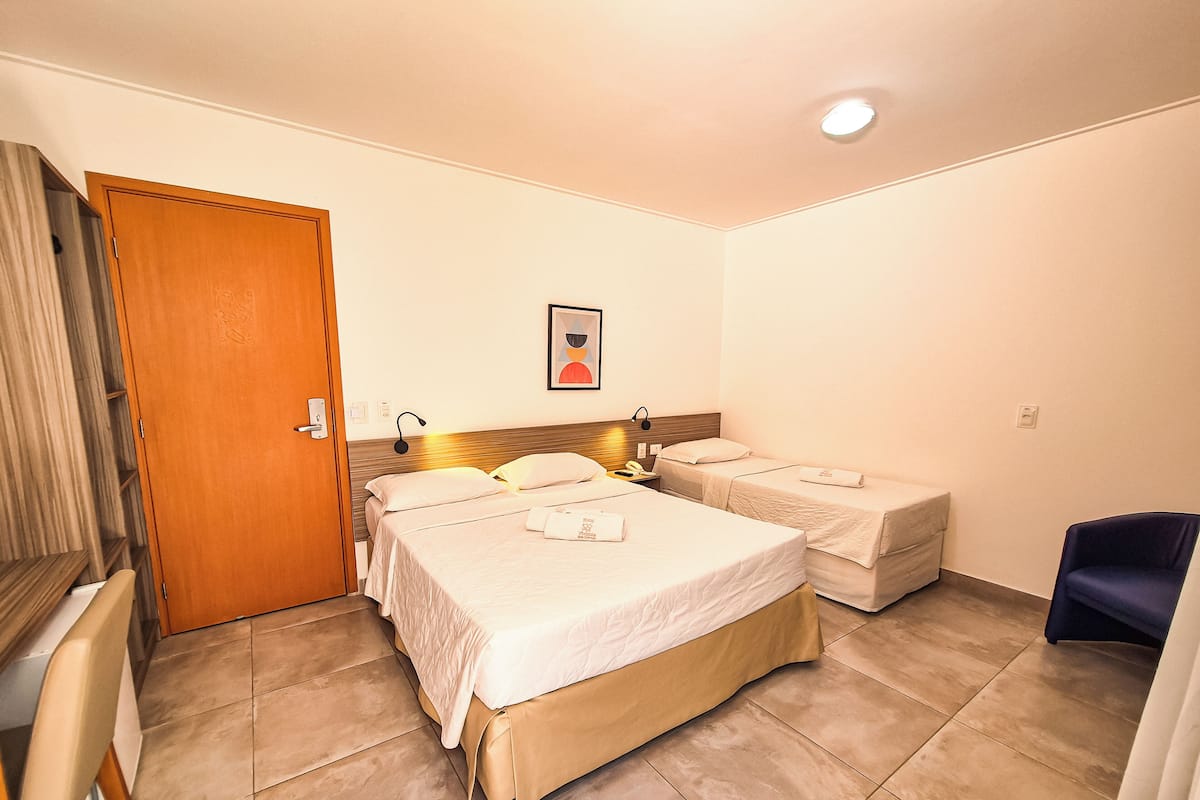 Habitación de hotel con dos camas individuales, un armario de madera, un escritorio con una silla y una pequeña silla azul.