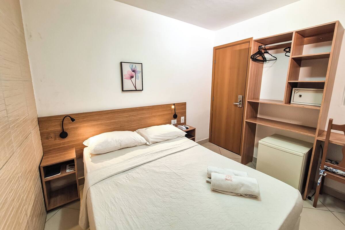 Habitación de hotel impecable con cama, mesitas de noche, armario y un pequeño escritorio con lámpara.