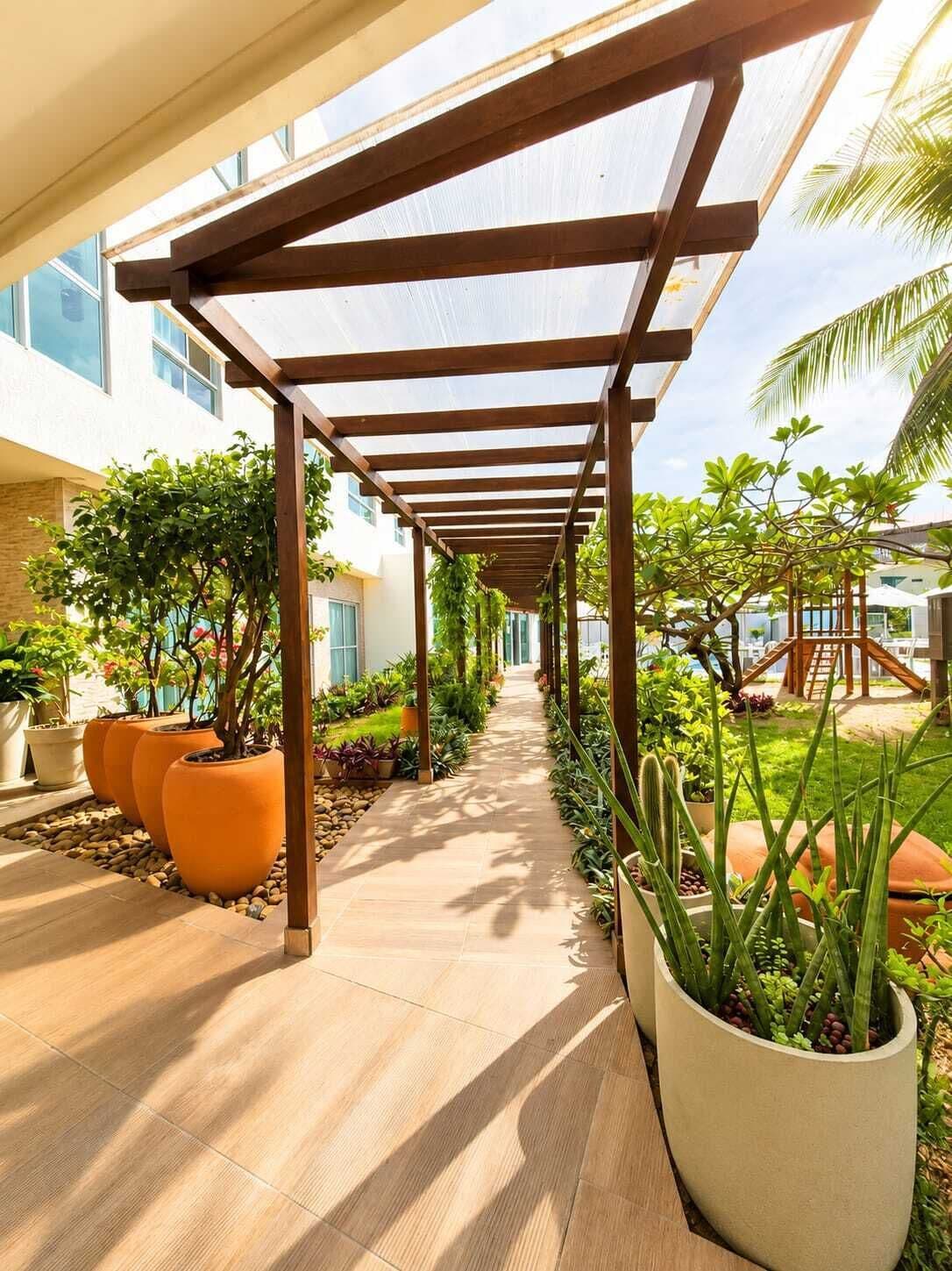 A covered walkway with potted plants, a clear sky, and a building in the background.