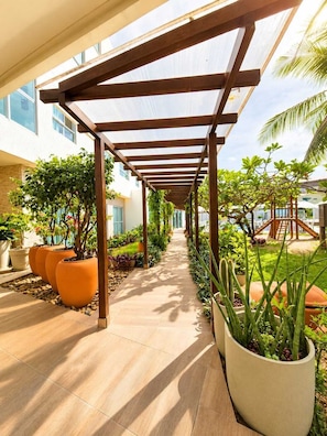 A covered walkway with potted plants, a clear sky, and a building in the background. - Vivenda dos Corais (Ipojuca)