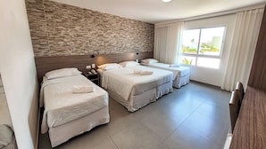 Habitación de hotel con tres camas, pared de piedra, ventana con cortinas y escritorio de madera.