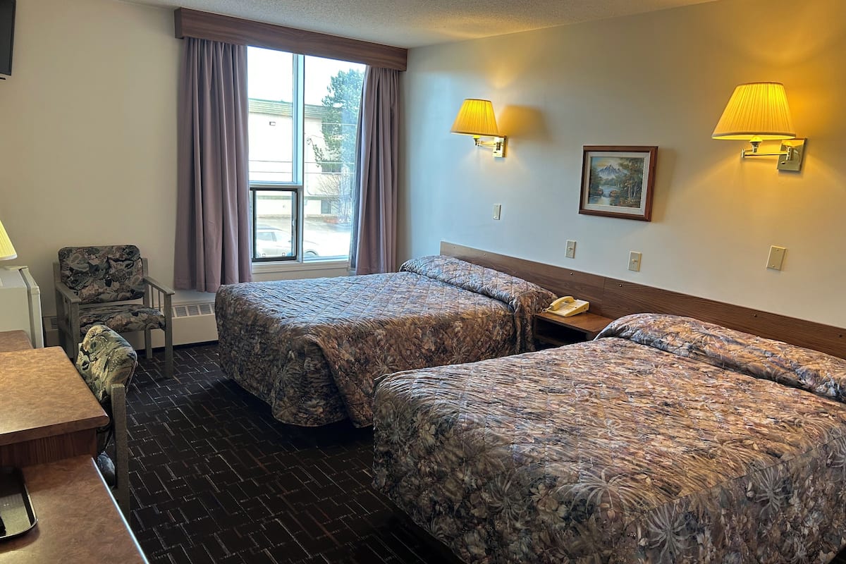 Habitación de hotel con dos camas, una silla, un escritorio, un teléfono y dos lámparas de pared.