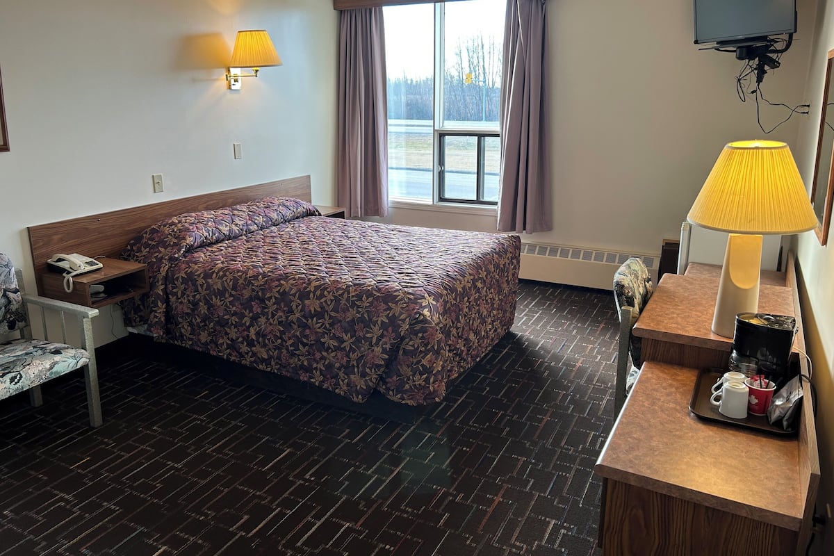 Habitación de hotel con cama, mesita de noche, lámpara y televisión montada en la pared.