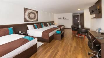 Habitación de hotel con tres camas, un escritorio, una silla, un televisor y piso de madera.