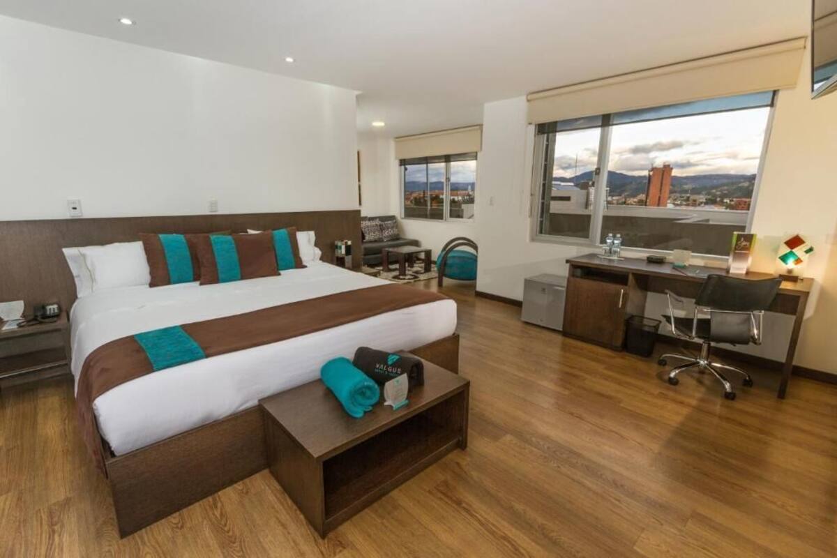 Habitación de hotel con una cama grande, un escritorio, una silla y vistas a la ciudad.