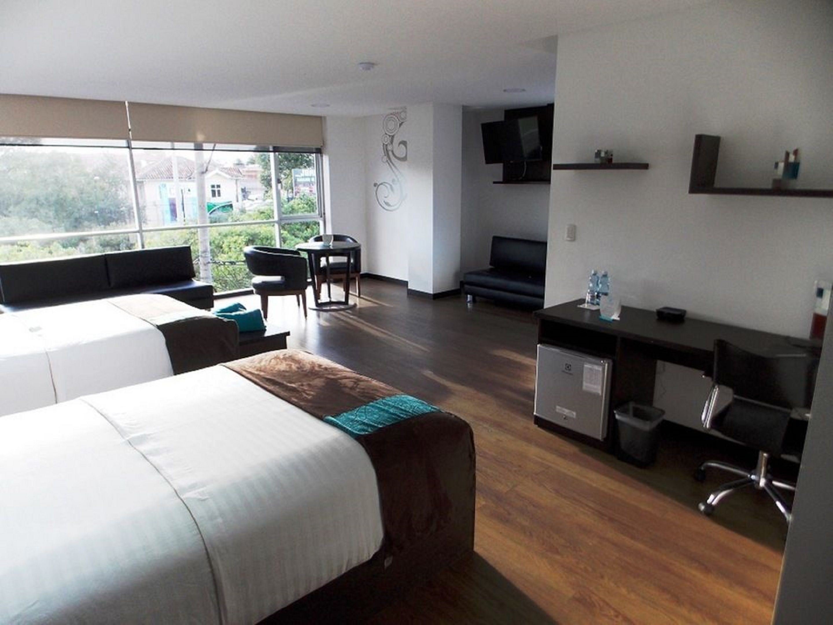 A modern hotel room with a large bed, a desk, a chair, and a TV.