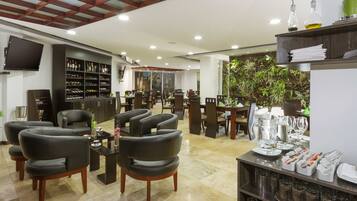 Un hall espacioso con sillones de cuero, una zona de bar con estantes llenos de botellas y un comedor con mesas y sillas.