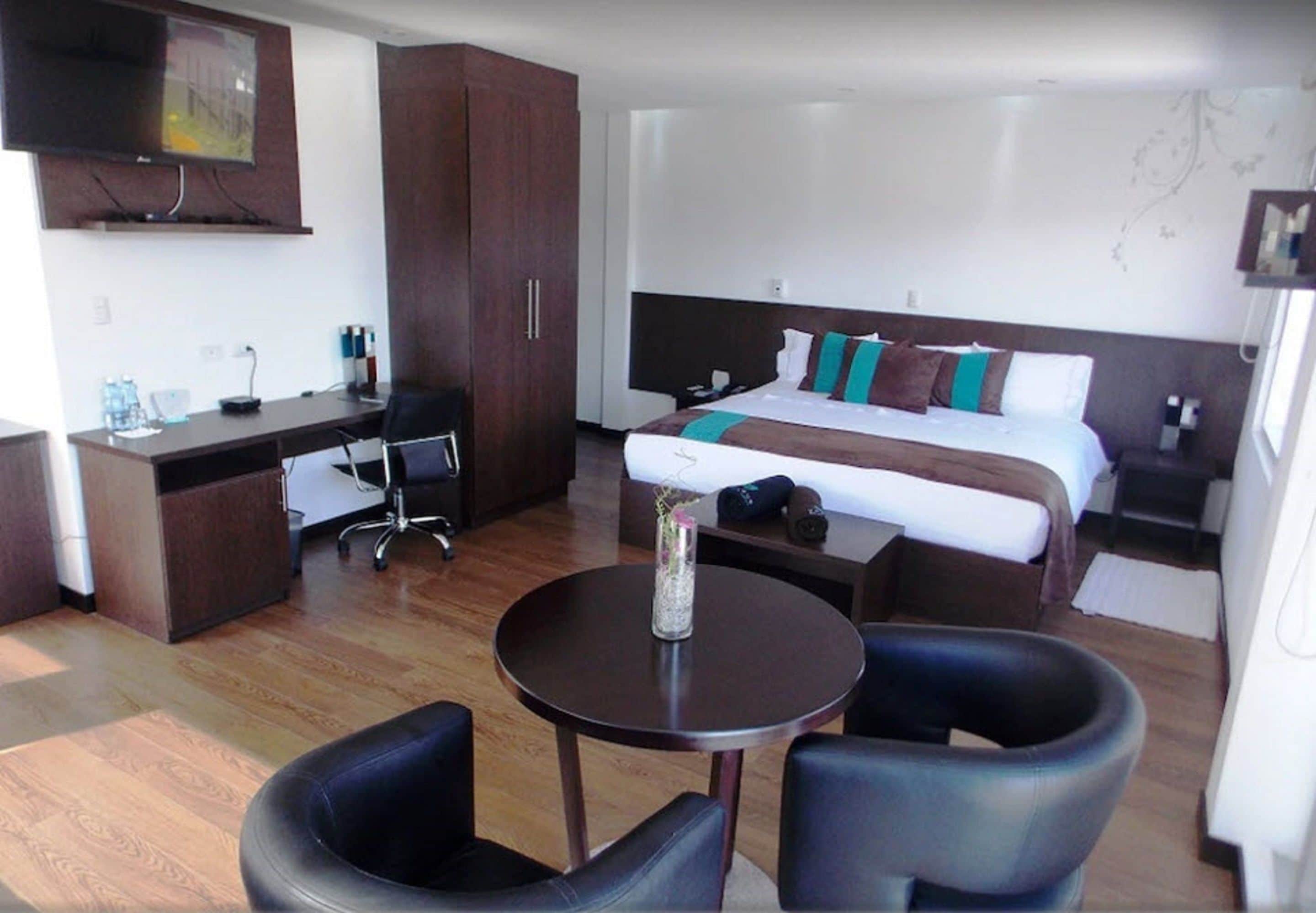 Una habitación de hotel con una cama, escritorio, sillas y televisión.